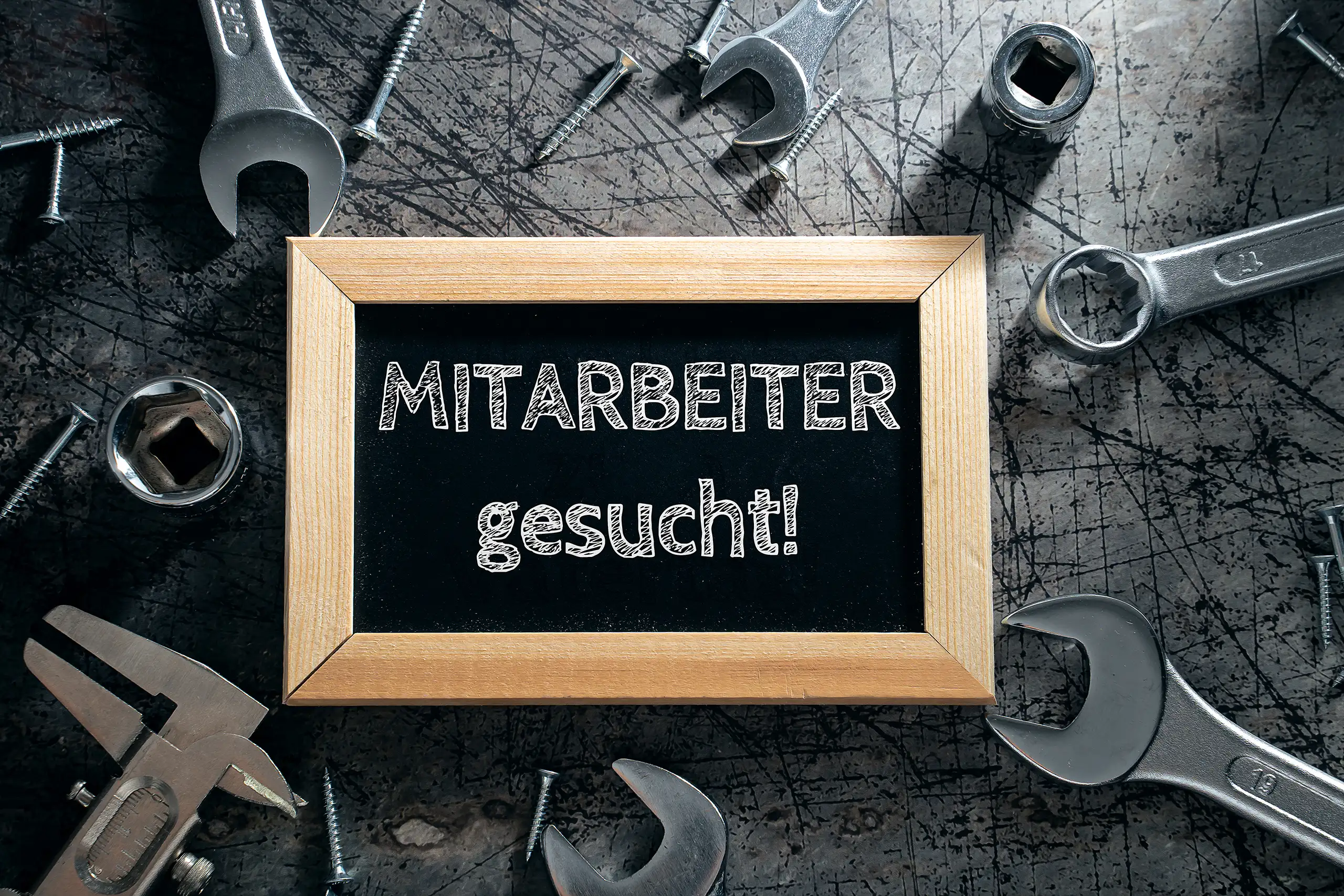 Kreidetafel mit der Aufschrift „Mitarbeiter gesucht!“, umgeben von Werkzeug